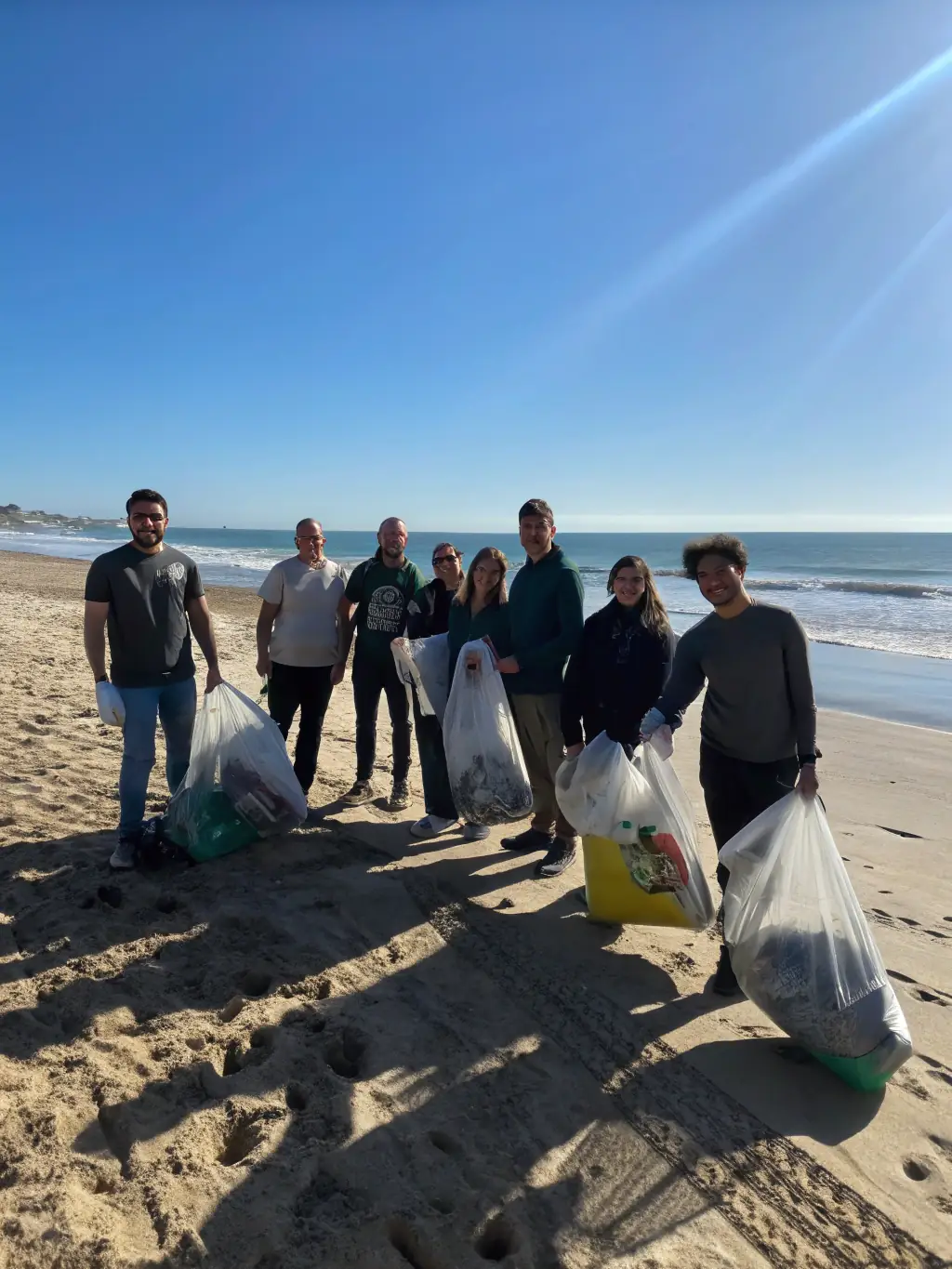 A photograph showcasing a group of volunteers cleaning up a beach, removing plastic waste and debris, with the ocean in the background.